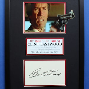 Puede incluir: Una fotografía enmarcada de Clint Eastwood como el inspector Harry Callahan de la película "El ejecutor". La foto muestra a Eastwood sosteniendo un arma y mirando intensamente a la cámara. El marco incluye una tarjeta de título con el título de la película y el nombre de Eastwood, así como una cita de la película: "Adelante, haz mi día."