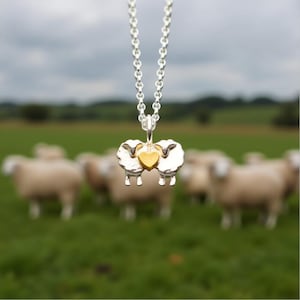 May include: A silver necklace with a charm of two silver sheep facing each other with a gold heart in between.