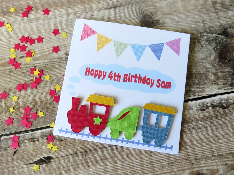 May include: A square white greeting card featuring a colorful bunting banner at the top and the text Happy 4th Birthday Sam in red letters inside a light blue cloud. A red, green, and blue train sits on a blue track at the bottom of the card.