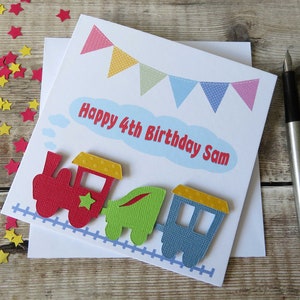 May include: A square white greeting card featuring a colorful train illustration with a red engine, green carriage, and blue caboose on a light blue track. Above the train, a light blue cloud contains the red text Happy 4th Birthday Sam.
