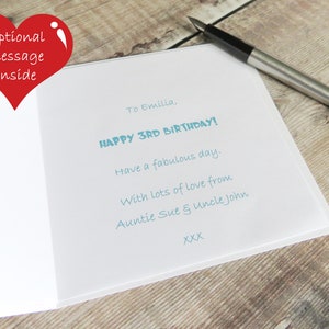 May include: A white greeting card with light blue printed text that reads: To Emilia, HAPPY 3RD BIRTHDAY! Have a fabulous day. With lots of love from Auntie Sue & Uncle John XXX. A black and silver fountain pen rests on the card.