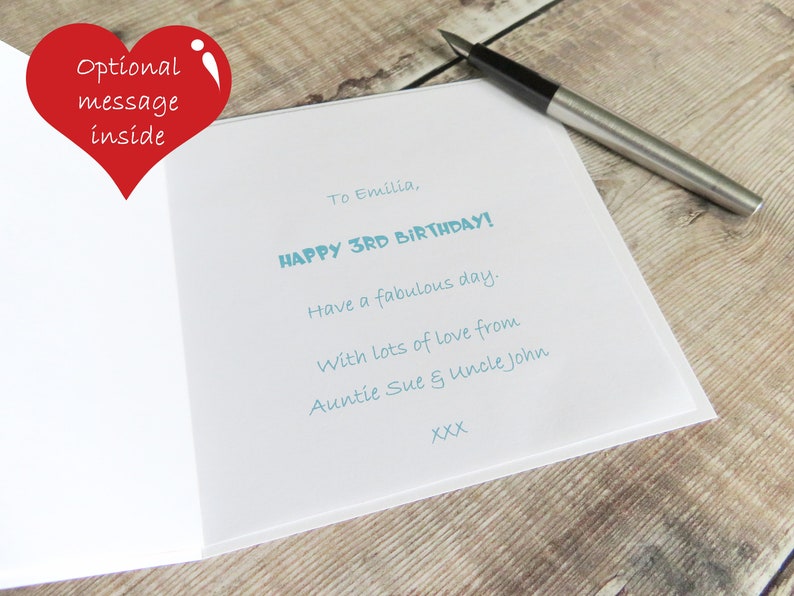 May include: A white greeting card with light blue printed text that reads: To Emilia, HAPPY 3RD BIRTHDAY! Have a fabulous day. With lots of love from Auntie Sue & Uncle John XXX. A black and silver fountain pen rests on the card.