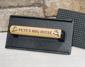 May include: A black cast iron grill press with a wooden handle. The handle has the text "Pete's BBQ House" printed on it.