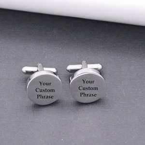 May include: A pair of silver cufflinks with a round, engraved surface. The engraving reads "Your Custom Phrase".