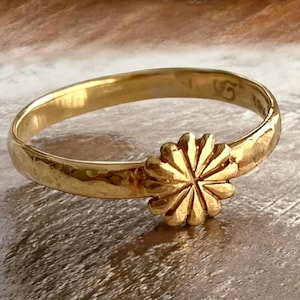 Könnte beinhalten: Ein goldener Ring mit gehämmerter Oberfläche und einem blütenförmigen Design. Die Blume hat ein Sternmuster.