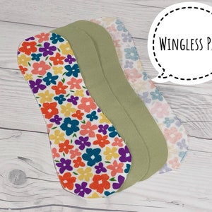 May include: Three reusable cloth pads with a floral print and a green pad. The pads are layered on top of each other. The text "WINGLESS PAD" is written in a speech bubble.