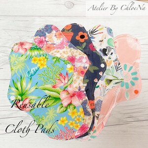 May include: A stack of five reusable cloth pads with floral patterns. The pads are in various colors, including blue, pink, white, and black. The text "Reusable Cloth Pads" is written on the bottom of the image.