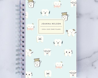 May include: A light blue planner with a clear plastic cover. The cover features a repeating pattern of cartoon teeth with various accessories, such as glasses, mustaches, and crowns. The planner is titled "JOANNA NELSON - 2024-2025 DMD PLANS - "