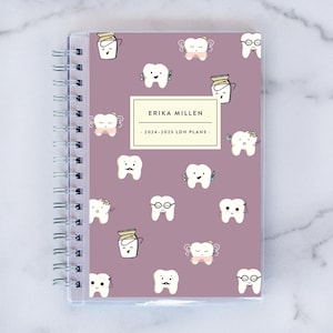May include: A purple planner with a clear plastic cover and a spiral binding. The cover features a repeating pattern of cartoon teeth with different expressions and accessories. The planner has the text "ERIKA MILLEN" and ". 2024-2025 LDH PLANS ." printed on the front.