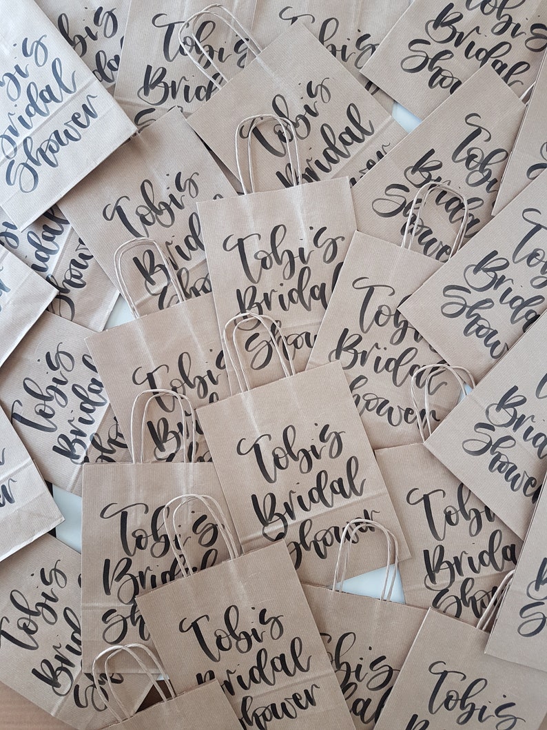 May include: A collection of brown paper gift bags with black calligraphy that reads "Tobi's Bridal Shower".