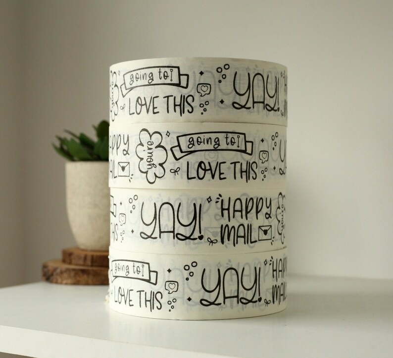 Puede incluir: Cuatro rollos de cinta washi blanca con letras negras. La cinta presenta las palabras "going to love this", "yay!" y "happy mail".