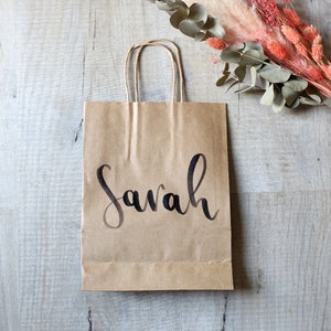 May include: A brown paper gift bag with a black handwritten name "Sarah" on the front.