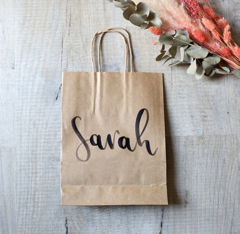 May include: A brown paper gift bag with a black handwritten name "Sarah" on the front.