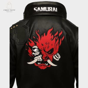 May include: Black leather jacket featuring a red and white graphic design on the back. The design is a stylized demon face. The word "SAMURAI" is printed in white on the collar. The jacket has shoulder accents with gold-colored studs.