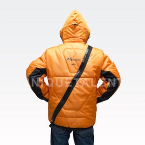 May include: Orange puffer jacket with a hood and black accents on the sleeves. The jacket has a black strap across the body and a logo on the back. The jacket is worn over blue jeans.