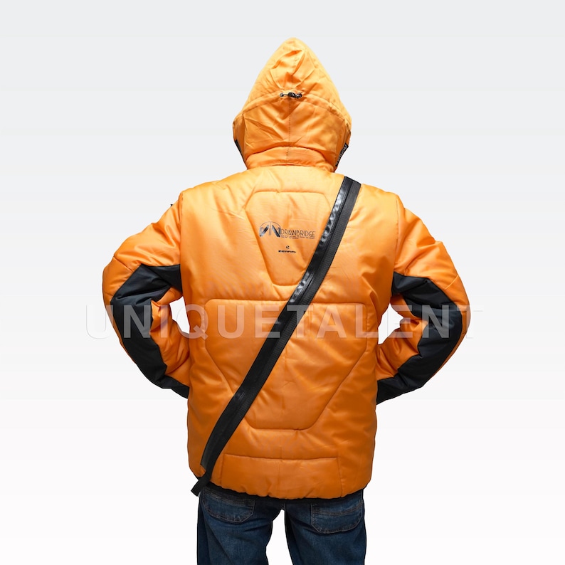 May include: Orange puffer jacket with a hood and black accents on the sleeves. The jacket has a black strap across the body and a logo on the back. The jacket is worn over blue jeans.