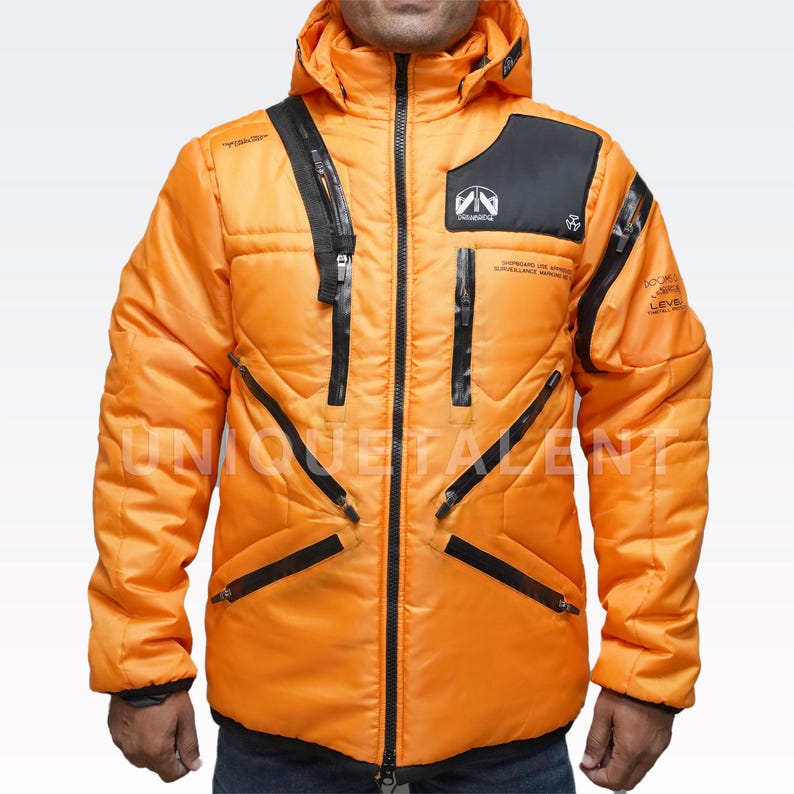 May include: Bright orange puffer jacket with a hood and black zippers. The jacket features the text "UNIQUE TALENT" and other text and logos. The jacket has a quilted design and a black panel on the upper chest.