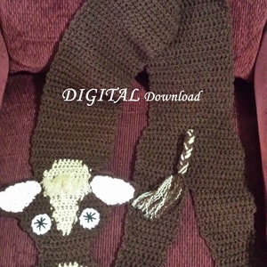 May include: Brown crocheted cow scarf with a white face and black eyes. The scarf has a brown tail and a brown body. The text "DIGITAL Download" is visible on the scarf.