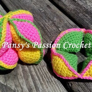 May include: Two colorful crochet toys in the image. One is a closed ball, and the other is an open, flower-like shape. The toys are made of bright pink, yellow, and green yarn. The text "Pansy's Passion Crochet" is visible on the toys.