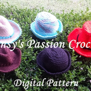 Puede incluir: Cinco sombreros tejidos a crochet en diferentes colores y estilos, incluyendo un fedora marrón, un fedora negro, un sombrero de vaquero rojo, un sombrero de sol azul claro y un sombrero de vaquero beige con ribete azul. Los sombreros están dispuestos sobre un lecho de follaje verde. El texto "Pansy's Passion Crochet" y "Digital Pattern" es visible en la imagen.