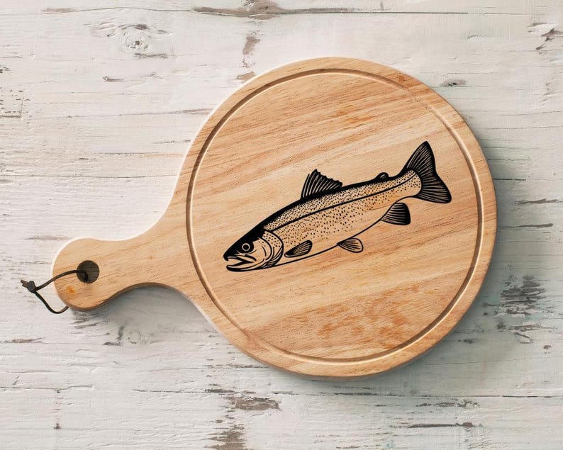 May include: Round wooden cutting board with a handle, featuring a detailed black illustration of a fish. The board has a natural wood grain finish and a small hole in the handle for hanging.