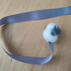 May include: A gray and white felt sheep bookmark with a gray ribbon.
