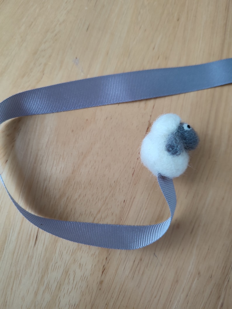 May include: A gray and white felt sheep bookmark with a gray ribbon.