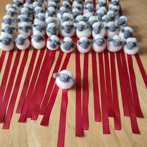 May include: A group of white felt sheep with gray faces are lined up on red ribbons. The sheep are all facing forward and have a single sheep in the center of the image.