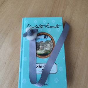 May include: A teal blue book with a gray ribbon bookmark and a small gray and white sheep figurine. The book cover features the text "Charlotte Bronte" and "Shirley" with a picture of a house.
