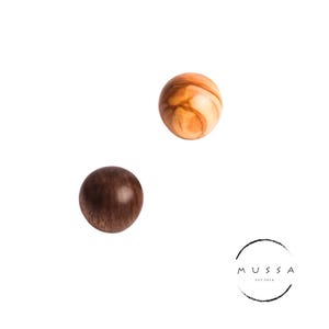 May include: Two spherical wooden objects, one featuring a light tan color with prominent swirling grain patterns and the other a solid dark brown color. A circular logo with the text MUSSA EST. 2016 is positioned in the lower right corner.