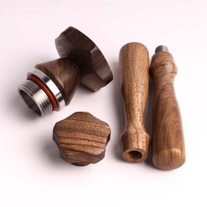 Op de afbeelding: Een set van vier houten koffie tamper tools. De tools zijn gemaakt van donkerbruin hout met een natuurlijk houtnerfpatroon. De set bevat een tamper basis, een tamper handvat en twee vervangende handvatten.