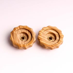 Puede incluir: Dos pomos de madera con un tornillo central de latón. Los pomos son de color marrón claro con un patrón de veta de madera.