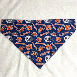 May include: A blue and orange dog bandana with a repeated pattern of Auburn Tigers logos, helmets, and the words "Auburn Tigers".