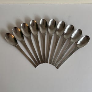 May include: A set of twelve silver spoons arranged in a fan shape. The spoons are all the same size and shape, with a rounded bowl and a long, slender handle.