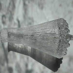 Puede incluir: Una jarra de vidrio transparente con una superficie texturizada y una boca ancha y acampanada. La jarra tiene un diseño único con una serie de protuberancias elevadas alrededor del borde.