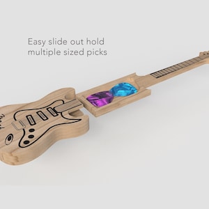 Puede incluir: Un soporte para púas de guitarra de madera con forma de guitarra, con un compartimento deslizable para guardar púas. El soporte tiene un contorno negro de una guitarra y la palabra "Frank" escrita en él. Se pueden ver dos púas en el compartimento, una morada y una azul.