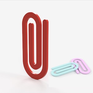 May include: Three paper clips, one red, one light blue, and one pink, are arranged on a white surface. The red paper clip is standing upright.