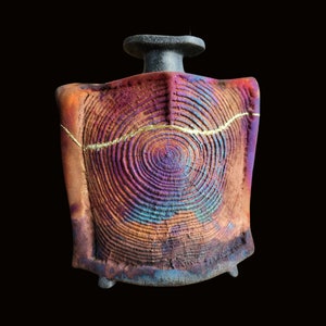 Op de afbeelding: Een keramische vaas met een uniek, getextureerd, cirkelvormig ontwerp in tinten paars, blauw en oranje. De vaas heeft een gouden accent en een zwarte basis.