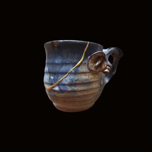 Peut inclure: Une tasse en céramique bleue et brune avec un glaçage craquelé doré et une anse sculptée. La tasse a un aspect rustique et fait main.
