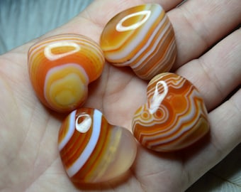 May include: Four heart-shaped agate stones with orange, white, and yellow banding. The stones are smooth and polished.