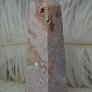 May include: A pink and white crystal obelisk with a textured surface. The obelisk has a rectangular base and tapers to a point. The crystal has a natural, organic appearance.