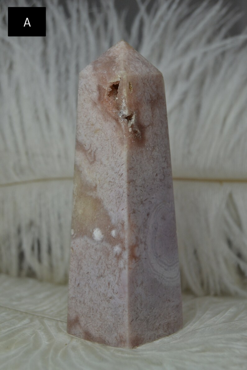 May include: A pink and white crystal obelisk with a textured surface. The obelisk has a rectangular base and tapers to a point. The crystal has a natural, organic appearance.