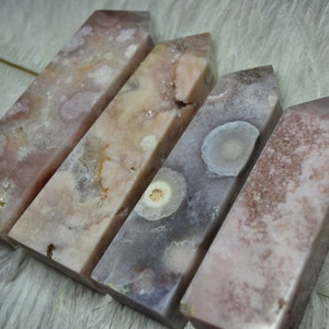 May include: Four pink and purple crystal obelisks with unique patterns and textures. The crystals have a polished, rectangular shape and vary in color from light pink to deep purple. The obelisks are arranged in a row, showcasing their natural beauty.