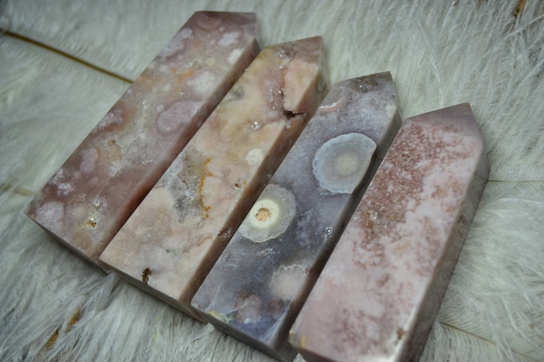 May include: Four pink and purple crystal obelisks with unique patterns and textures. The crystals have a polished, rectangular shape and vary in color from light pink to deep purple. The obelisks are arranged in a row, showcasing their natural beauty.