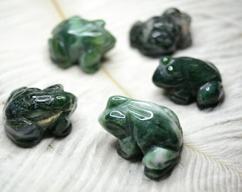 May include: Five green agate frog figurines on a white feathery surface. The frogs are carved from green agate with white and brown markings.
