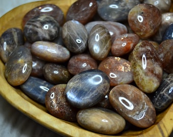 May include: A bowl of sunstone tumbled stones. The stones are a mix of brown, orange, and gold colors with a shimmery, iridescent finish.