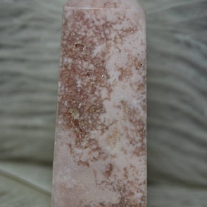 May include: A pink and brown crystal tower with a pointed top. The crystal has a unique pattern of brown and white veining throughout. The tower is a decorative item, likely used for display or spiritual purposes.