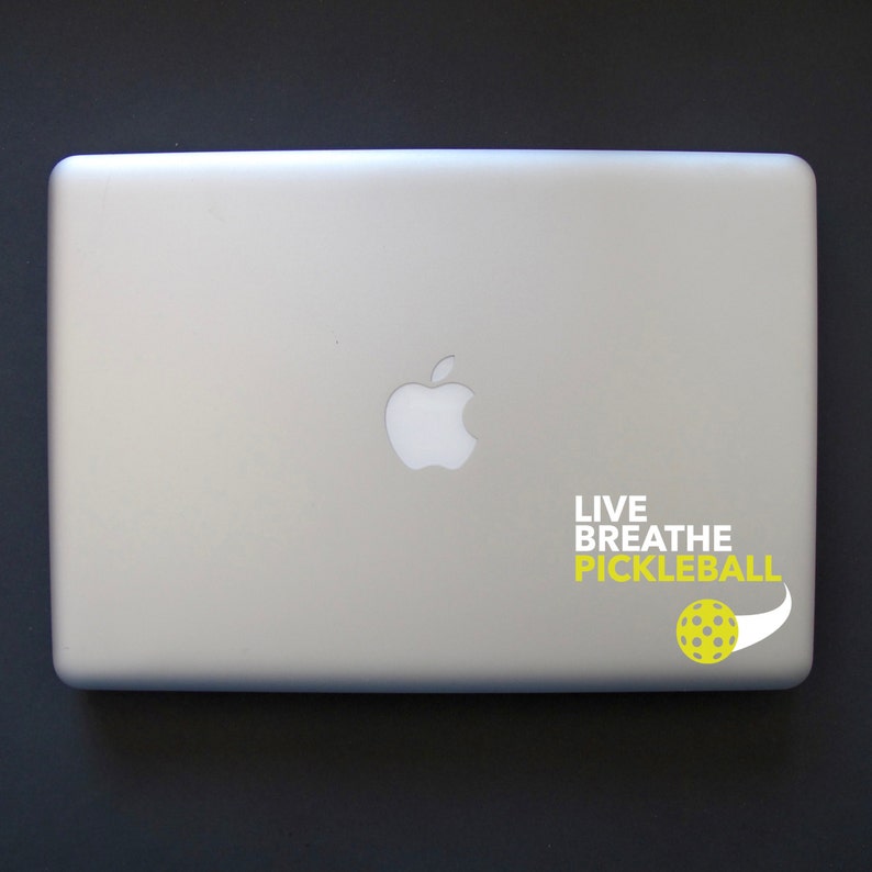 K&ouml;nnte beinhalten: Ein silberner Laptop mit einem wei&szlig;en Apple-Logo und einem gelben und wei&szlig;en Aufkleber mit der Aufschrift "Live Breathe Pickleball" und einer gelben Pickleball-Grafik.