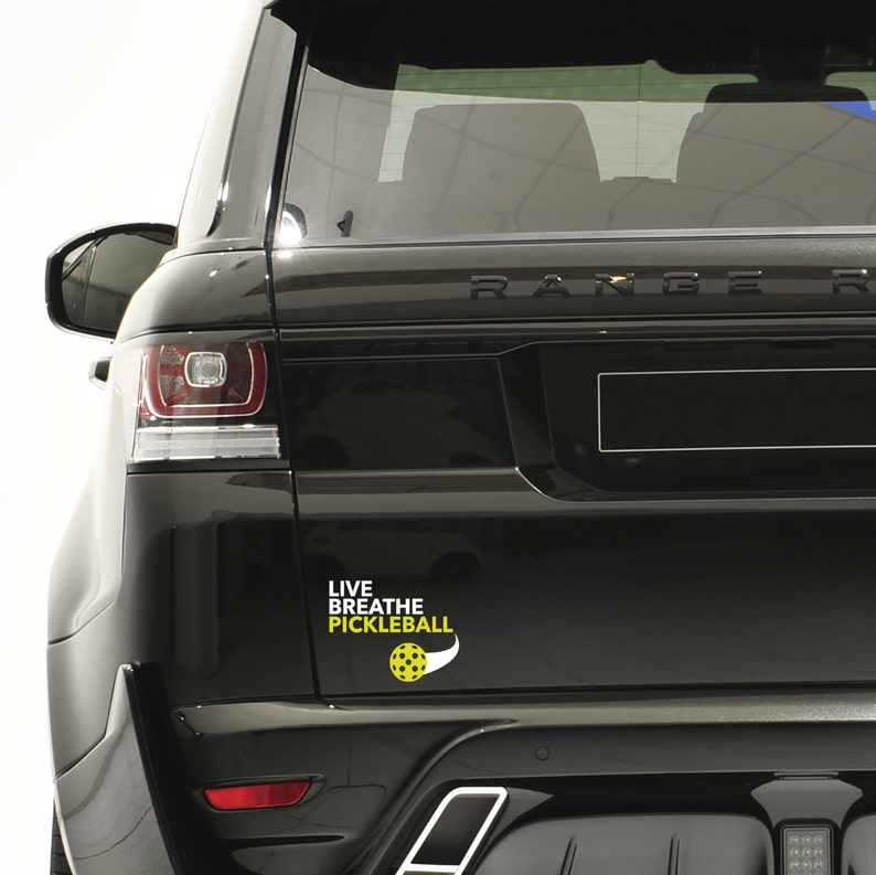 K&ouml;nnte beinhalten: Schwarzer SUV mit einem wei&szlig;en Vinyl-Aufkleber auf der R&uuml;ckseite, auf dem "Live Breathe Pickleball" mit einer gelben Pickleball-Grafik steht.