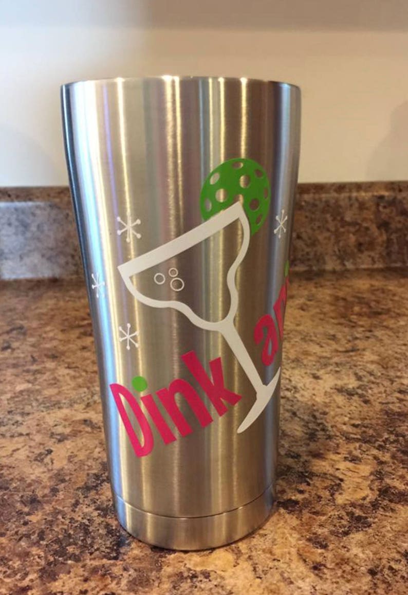 May include: Stainless steel tumbler with a pink "Dink and" text and a white margarita glass with a green lime wedge. The tumbler has a white snowflake design.